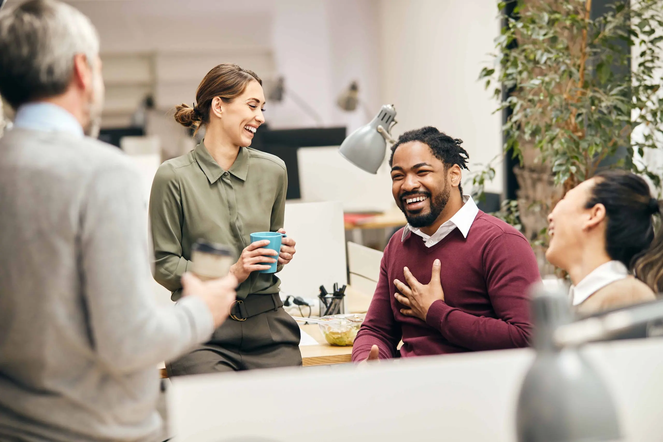 co workers laughing together in the office on break at their cubicle. 